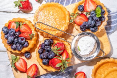 Yaz meyveli mini tart kekleri. Porsiyonlu vanilyalı tatlı bardakları taze çilek, yabanmersini, ahududu, beyaz ahşap arka plan fotokopi alanı