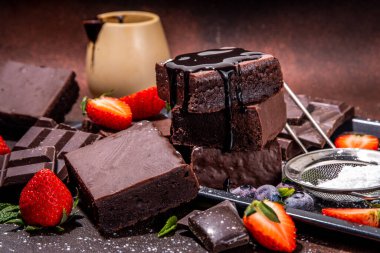 Böğürtlenli siyah çikolatalı kek. Üzerine çikolata sosu serpiştirilmiş ev yapımı kek kurabiyeleri ve koyu arkaplanda taze çilek, yabanmersini, fotokopi alanı.