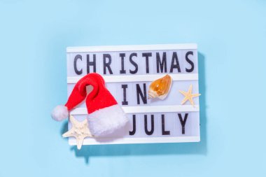 Temmuz tatilinde Noel ya da satış geçmişinde. Yaz tatili aksesuarları, deniz yıldızları, Noel Baba şapkalı şezlong, tropikal yapraklar. Kış tatilinde kaçamak, üst görünüm kopyalama alanı 