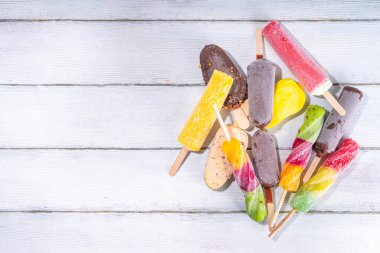Beyaz ahşap arka planda dondurmalı dondurma, yaz tatlıları, tatlı, tatil ve tatil geçmişi, çeşitli aromalı lolipoplar - çikolata, vanilya, meyve, gökkuşağı 