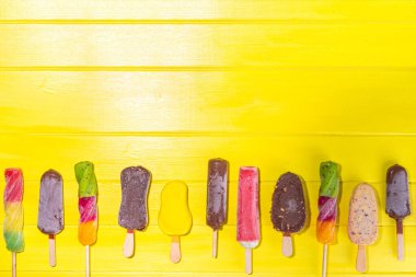 Yüksek renkli sarı arka planda dondurmalı dondurma, yaz tatlıları, tatlı, tatil ve tatil geçmişi, çeşitli aromalı lolipoplar - çikolata, vanilya, meyve, gökkuşağı 