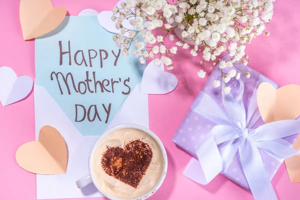 Mother day pastel colored pink flatlay with gifts, heart decorated coffee cup, flowers, note inscription Happy Mothers Day. Moms international holiday greeting card background top view copy space