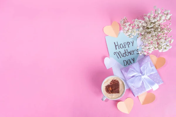 Mother day pastel colored pink flatlay with gifts, heart decorated coffee cup, flowers, note inscription Happy Mothers Day. Moms international holiday greeting card background top view copy space