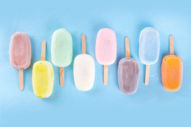 Çok renkli dondurmalı buzlu dondurma seçimi. Çeşitli aromalı dondurmalar, dondurulmuş lolipoplar. Açık mavi arka planda çikolatalı, vanilyalı, böğürtlenli, şam fıstığı portakalı.