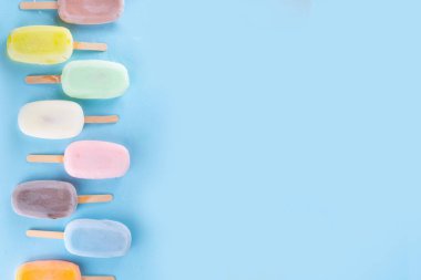 Çok renkli dondurmalı buzlu dondurma seçimi. Çeşitli aromalı dondurmalar, dondurulmuş lolipoplar. Açık mavi arka planda çikolatalı, vanilyalı, böğürtlenli, şam fıstığı portakalı.