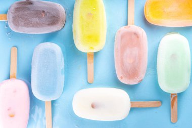 Çok renkli dondurmalı buzlu dondurma seçimi. Çeşitli aromalı dondurmalar, dondurulmuş lolipoplar. Açık mavi arka planda çikolatalı, vanilyalı, böğürtlenli, şam fıstığı portakalı.