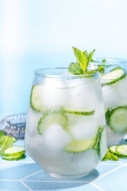 Ferahlatıcı yaz içeceği. Nane şekeri, salatalık, limon kokteyli. Açık mavi fayanslı masa, parlak güneş ışığı, kopyalama alanı. İki bardak salatalıklı su ya da limonata, sağlıklı diyet içecek.