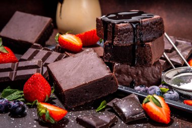 Böğürtlenli siyah çikolatalı kek. Üzerine çikolata sosu serpiştirilmiş ev yapımı kek kurabiyeleri ve koyu arkaplanda taze çilek, yabanmersini, fotokopi alanı.