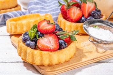 Yaz meyveli mini tart kekleri. Porsiyonlu vanilyalı tatlı bardakları taze çilek, yabanmersini, ahududu, beyaz ahşap arka plan fotokopi alanı