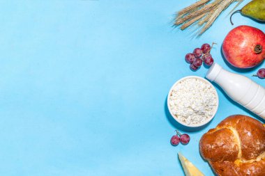 Yahudi bayramının sembolleri olan mutlu Shavuot tebrik kartı - nar, üzüm, elma, tatlı challah ekmeği, buğday filizi, süt, peynir, süzme peynir, açık mavi zemin