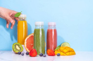  Portakal şişelerinde yeşil, portakal ve kırmızı smoothie, farklı meyvelerden oluşan renkli sağlıklı meyve suyu karışımı: portakal, greyfurt, limon, kivi, çilek, malzemelerle birlikte.