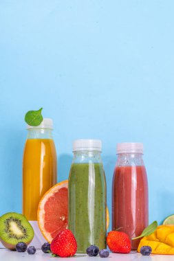  Portakal şişelerinde yeşil, portakal ve kırmızı smoothie, farklı meyvelerden oluşan renkli sağlıklı meyve suyu karışımı: portakal, greyfurt, limon, kivi, çilek, malzemelerle birlikte.