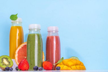  Portakal şişelerinde yeşil, portakal ve kırmızı smoothie, farklı meyvelerden oluşan renkli sağlıklı meyve suyu karışımı: portakal, greyfurt, limon, kivi, çilek, malzemelerle birlikte.