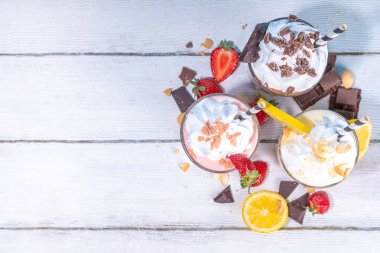 Yaz tazeleyici milkshake seti ya da klasik lezzetli tadı olan meyve suları vanilya limonu, çilek, çikolata, krem şanti ve malzemelerle beyaz, açık mavi, güneşli bir arka planda. 