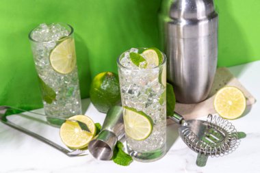 Klasik yaz soğuk mojito kokteyli, limonlu limonata, nane, ezilmiş buz ve beyaz arka planda bar aletleri.