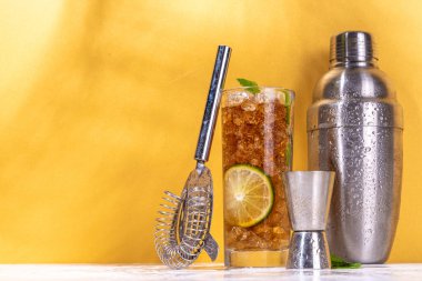  Küba libre ya da Long Island yaz kokteyli, limonlu ve naneli buzlu kola. Buzlu, uzun ve alkollü bir içecek, ezilmiş buz ve altın bej arka planda bar aletleri. 