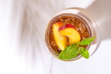 Buzlu şeftali çayı, ya da limonlu şeftali limonatası, nane, ezilmiş buz ve altın bej arka planda bar aletleri. 