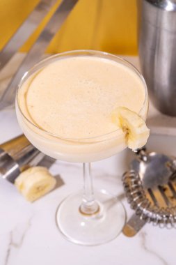 Tatlı yaz soğuk muz kokteyli ya da martini kokteyli, muzlu likör, dilimler, ezilmiş buz ve altın bej arka planda bar aletleri. 