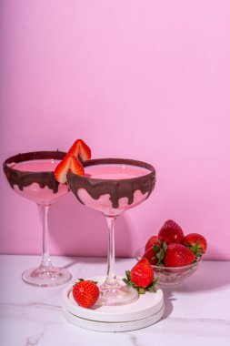 Tatlı çikolatalı çilek kokteyli, şirin pembe çilekli martini ya da daiquiri kremalı içecek, taze çilekli garnitür ve çikolatalı çiseleme, açık pembe arka planda.