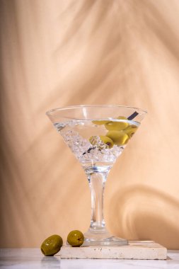 Klasik sek martini kokteyli, yeşil zeytinli, bej renkli arka planda.