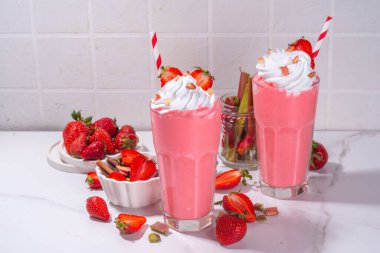 Rubarb ve çilekli milkshake veya smoothie, ferahlatıcı yaz içeceği, sağlıklı diyet ve antioksidan yaz içeceği kremalı, taze ravent, çilek dilimleri, beyaz mutfak masasında.