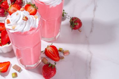 Rubarb ve çilekli milkshake veya smoothie, ferahlatıcı yaz içeceği, sağlıklı diyet ve antioksidan yaz içeceği kremalı, taze ravent, çilek dilimleri, beyaz mutfak masasında.