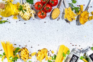 Beyaz masa arkasında çeşitli kurutulmuş spagetti, makarna ve kaşıklarla hazırlanmış makarna. Farklı şekillerde çiğ İtalyan makarnası, otlar, zeytinyağı, domatesler, baharatlar.