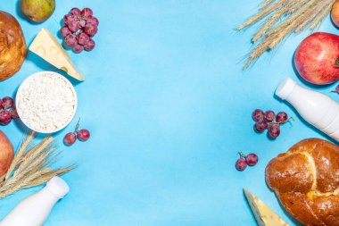 Yahudi bayramının sembolleri olan mutlu Shavuot tebrik kartı - nar, üzüm, elma, tatlı challah ekmeği, buğday filizi, süt, peynir, süzme peynir, açık mavi zemin