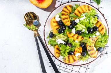 Summer peach salad. Fresh raw green salad with lettuce, arugula, grilled peach wedges, blueberry, feta cheese and honey