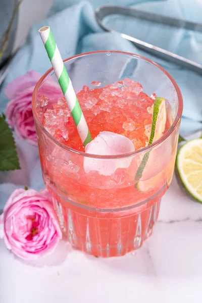 Rose flower lemonade, refreshing summer drink with crushed ice, rose petals and syrup, lime slices. Light rose cocktail, sour rose wine