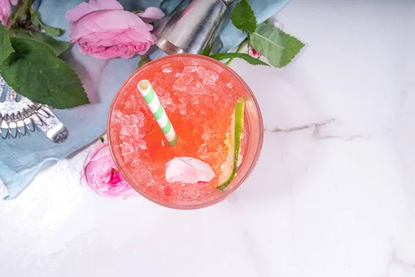 Rose flower lemonade, refreshing summer drink with crushed ice, rose petals and syrup, lime slices. Light rose cocktail, sour rose wine