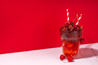 Buzlu vişneli kola, soğuk yaz meyveli alkolsüz kokteyl taze kirazlar, meyve suyu, kola ve buz, renkli arka plan fotokopi alanı.