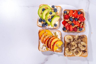 Meyveli sandviç. Fıstık ezmeli, krem peynirli çeşitli tostlar, yaz meyveleri ve meyveli çikolata - çilek, muz, şeftali, elma, yabanmersini, lezzetli öğle yemeği