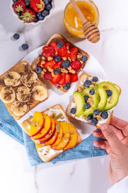 Meyveli sandviç. Fıstık ezmeli, krem peynirli çeşitli tostlar, yaz meyveleri ve meyveli çikolata - çilek, muz, şeftali, elma, yabanmersini, lezzetli öğle yemeği