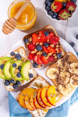 Meyveli sandviç. Fıstık ezmeli, krem peynirli çeşitli tostlar, yaz meyveleri ve meyveli çikolata - çilek, muz, şeftali, elma, yabanmersini, lezzetli öğle yemeği