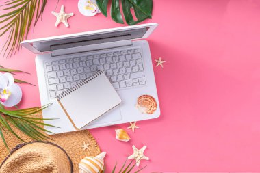 Yazlık ofis, çalışma geçmişi, blogcu iş yeri düzlüğü. Not defteri, hasır şapka, tropikal dekor ve yapraklarla dolu beyaz dizüstü bilgisayar klavyesi, açık pembe arka planda soğuk kokteyl bardağı.