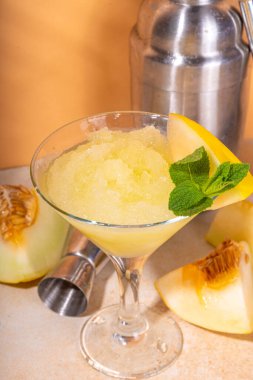 Kavunlu, limonlu ve naneli yaz likörü. Donmuş kavun martinisi ya da bardaklı kokteyl, bej renkli, güneşli arka planda.