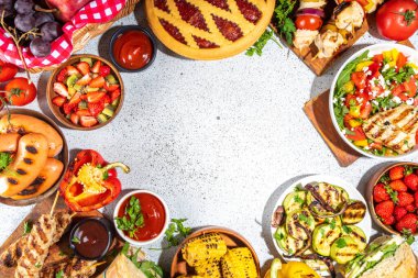 Çeşitli piknik barbekü yemekleri ve flatlay içiyorlar. Yaz bbq piknik yemekleri, ızgara etler, kebaplar, sebzeler, meyve salatası, geleneksel piknik pastası, sandviçler, üst görünüm fotokopi alanı.