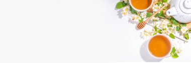 Organik bitkisel sağlık içeceği. Yasemin çiçekleri yeşil çay, beyaz kupalar, çaydanlık, beyaz masa, çiçek açan yasemin çiçekleri 