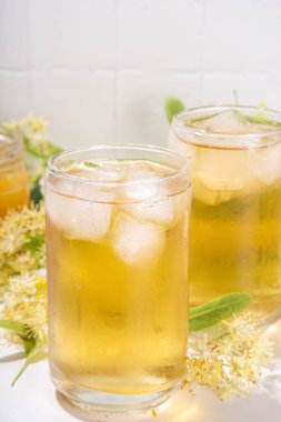 Organik bitkisel sağlık içeceği. Linden çiçeği yeşili çay, beyaz kupalar, çaydanlık, beyaz bir masa, kopya alanı ve çiçek açan ıhlamur çiçekleri