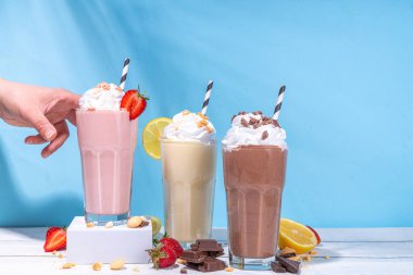Yaz tazeleyici milkshake seti ya da klasik lezzetli tadı olan meyve suları vanilya limonu, çilek, çikolata, krem şanti ve malzemelerle beyaz, açık mavi, güneşli bir arka planda. 