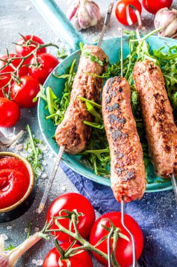 Şişe şiş kebap, kıyma etinden. Lula kebap, geleneksel Kafkas tarifi. Mavi beton arka planda, soslar, domatesler ve sebze salatası üst görünüm fotokopi alanı