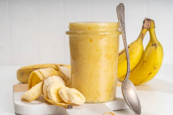 Bananas jam in small glass jar with fresh bananas on  white table background