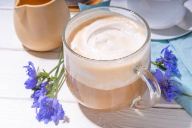  Chicory bitkisel kahve latte, cappuccino içecek, beyaz ahşap masada çırpılmış sütsüz süt ve mavi çiçekler. Alternatif vegan ve keto diyeti kahvesi, hindiba çiçekleri ve kök tozu. 