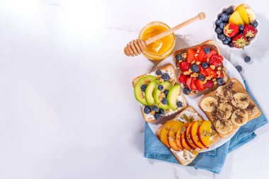 Meyveli sandviç. Fıstık ezmeli, krem peynirli çeşitli tostlar, yaz meyveleri ve meyveli çikolata - çilek, muz, şeftali, elma, yabanmersini, lezzetli öğle yemeği