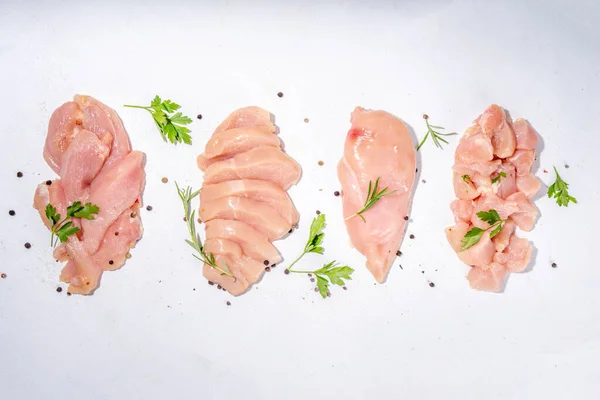 Chicken, turkey, white meat breast fillet on kitchen table, top view copy space. Different types of cutting meat. Strips, chopped, steak, cubes, whole breast, ready for cooking, with spices and herbs