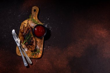 Grilled meat steak on dark table, Pork, veal, lamb, beef steak medium, medium well on cutting board, with spices, ketchup bbq sauce, wine glass. Dinner in steak restaurant menu, top view copy space