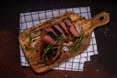 Grilled meat steak on dark table, Pork, veal, lamb, beef steak medium, medium well on cutting board, with spices, ketchup bbq sauce, wine glass. Dinner in steak restaurant menu, top view copy space