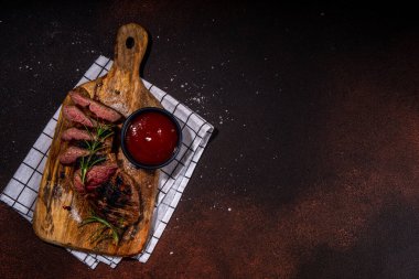 Grilled meat steak on dark table, Pork, veal, lamb, beef steak medium, medium well on cutting board, with spices, ketchup bbq sauce, wine glass. Dinner in steak restaurant menu, top view copy space