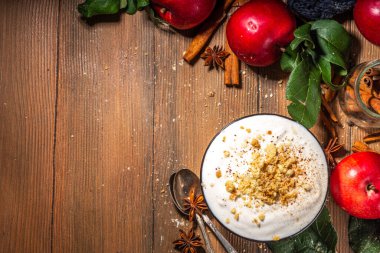 Bir kase ev yapımı elmalı turtalı yoğurt kahvaltıya hazır, üstüne de tart parçacıklı. Ahşap arka planda kırmızı sonbahar elmaları ve baharatları, kopyalama alanı